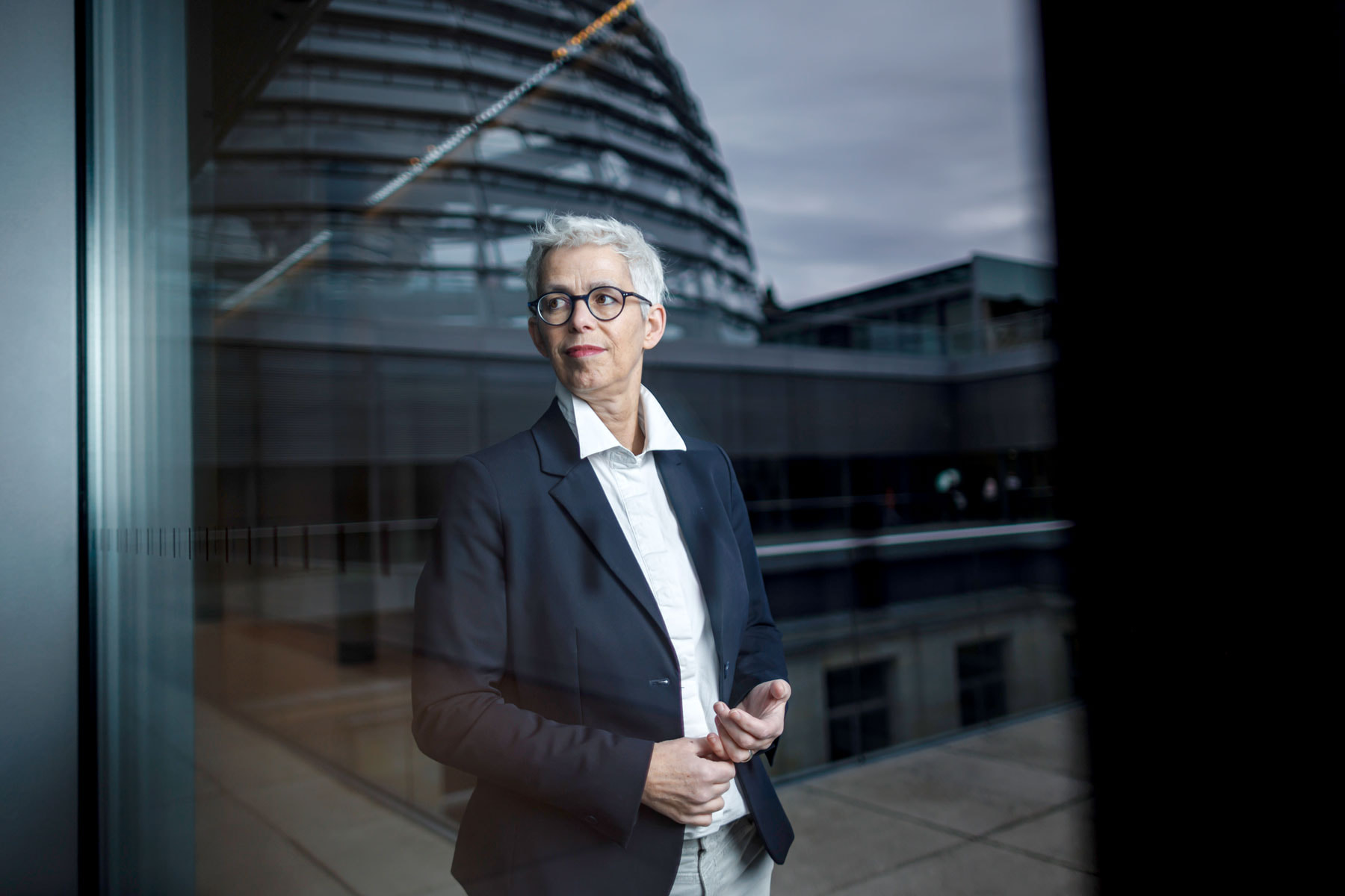 Ulle in dunklem Sakko steht vor einem Gebäude mit Kuppel, sichtbar durch ein Fenster
