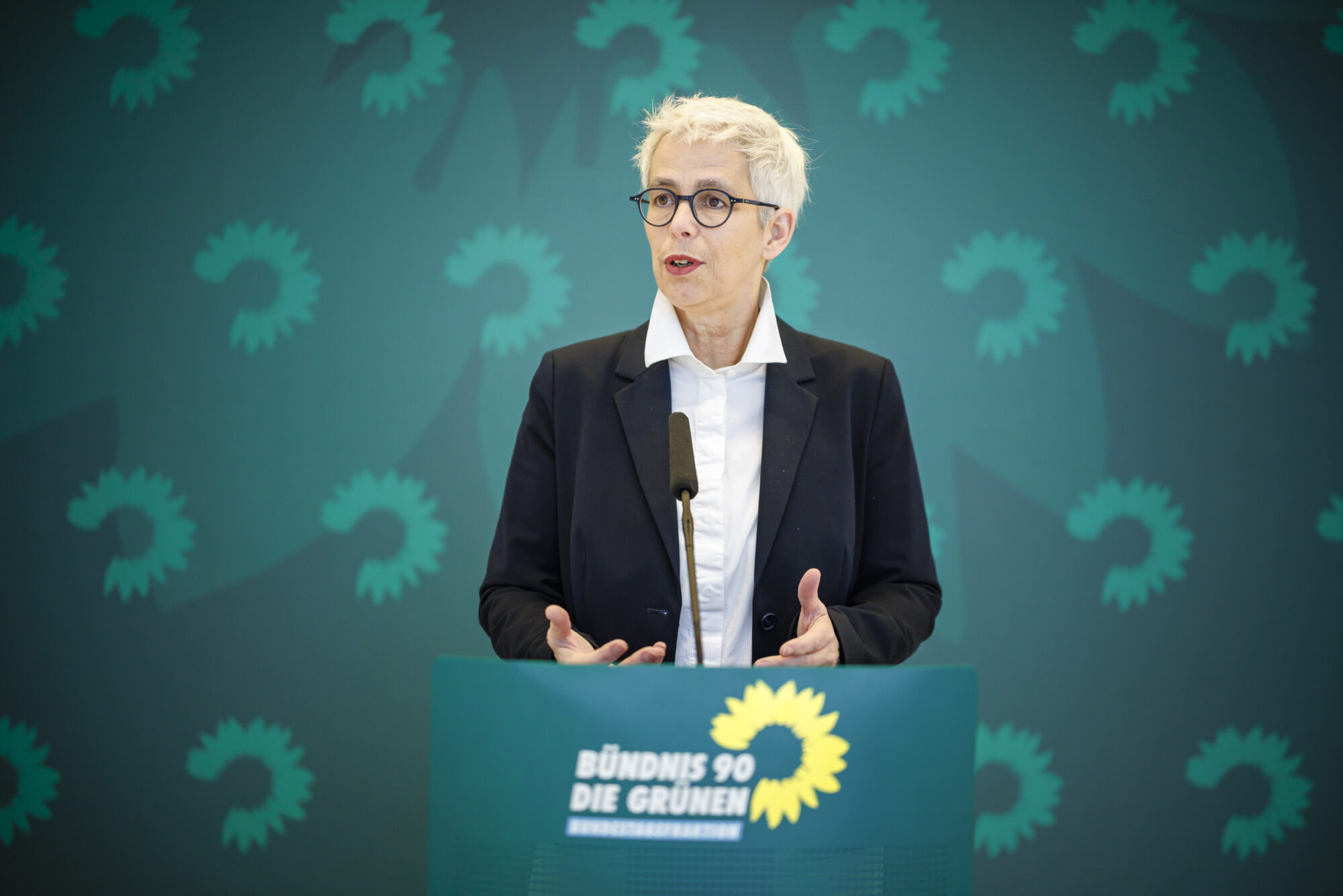 Ulle Schauws steht in einem dunklen Blazer am grünen Redepult der Grünen Bundestagsfraktion