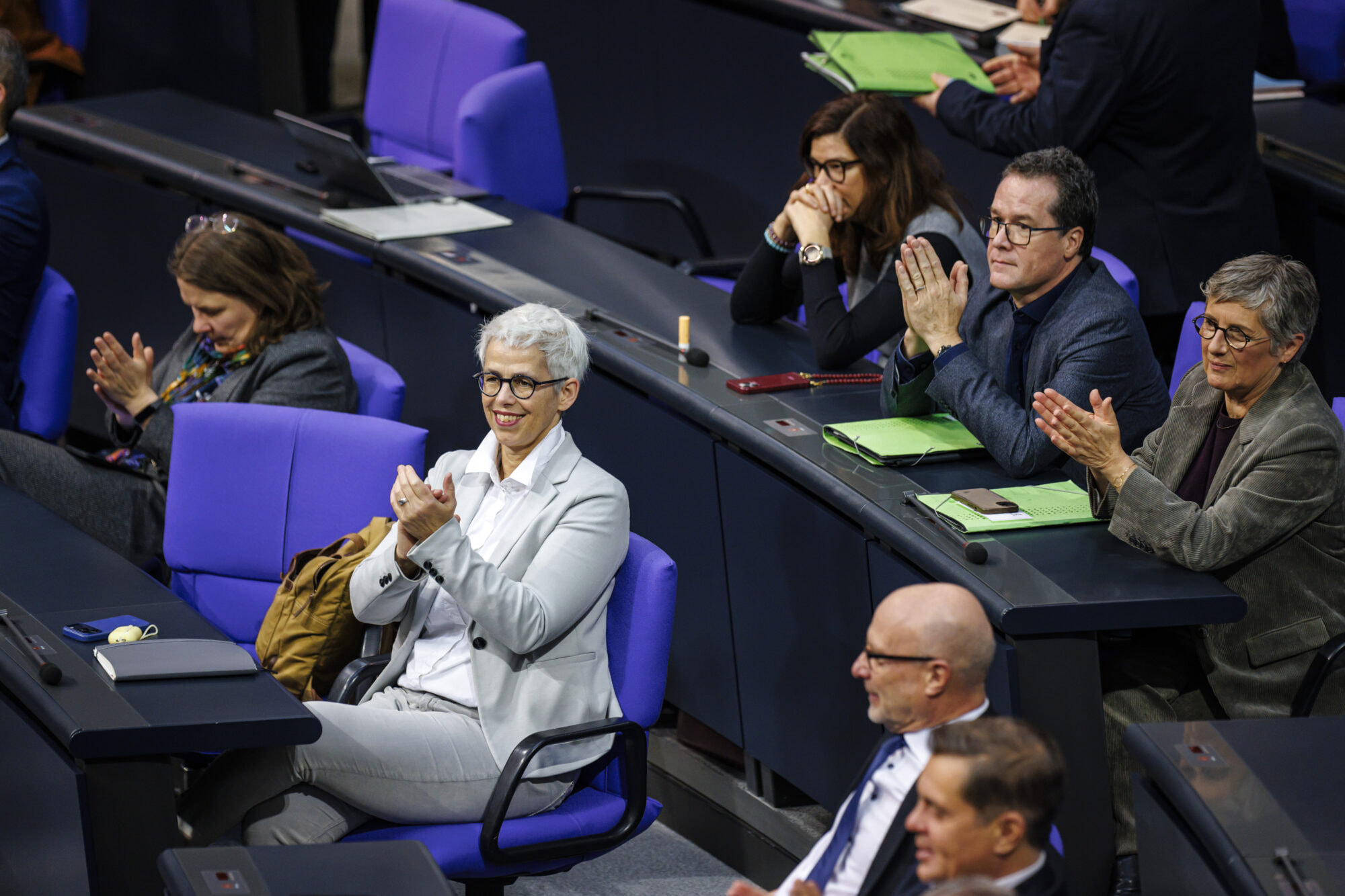 Ulle Schauws sitzt im Plenarsaal des Deutschen Bundestags und klatscht in die Hände