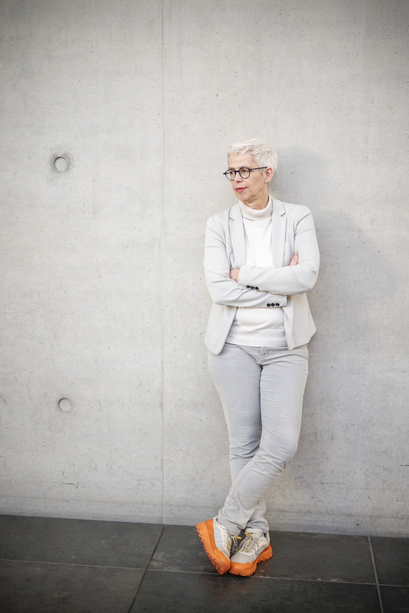Ulle Schauws lehnt in einem hellen Blazer an einer ebenfalls hellen Wand