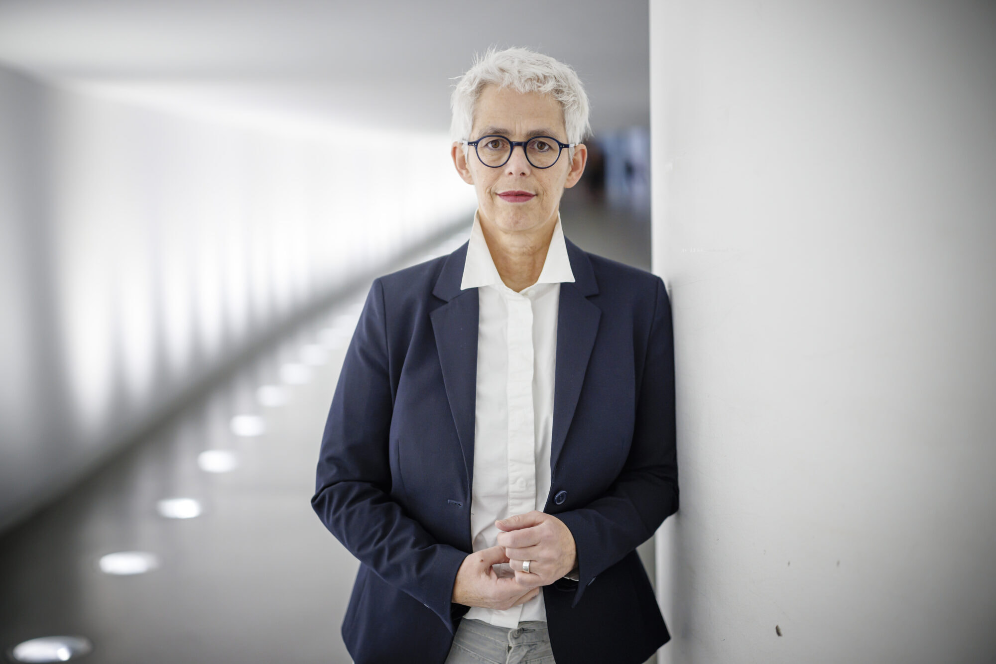 Ulle Schauws trägt einen blauen Blazer und lehnt an einer Säule