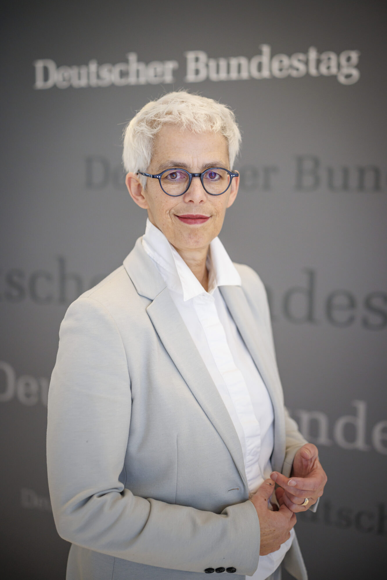 Ulle Schauws steht in einem grauen Blazer vor einer Pressewand des Deutschen Bundestages